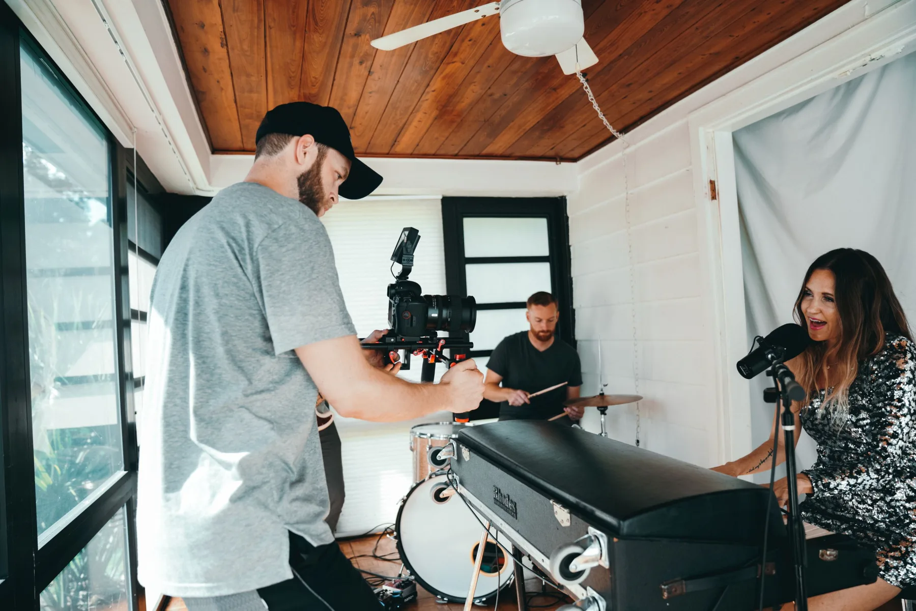 Un vidéaste filme une chanteuse au piano, avec son batteur en arrière-plan